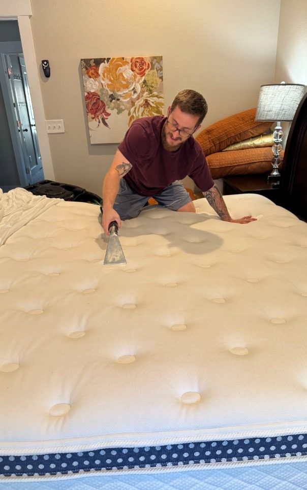 Person smoothing a mattress on a bed in a well-lit room.